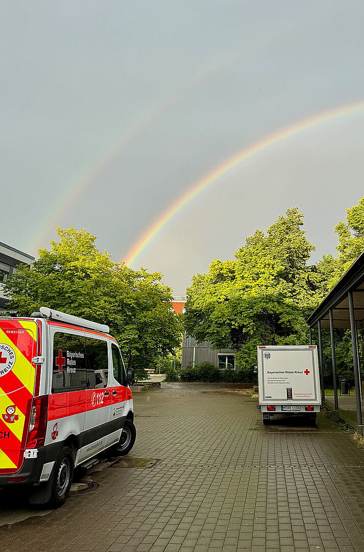Die Einsatzfahrzeuge der SEG Betreuung München bei einem Einsatz unter einem Regenbogen